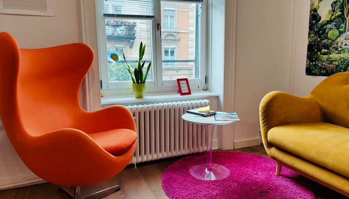 Wartezimmer mit orangem Sessel, gelbem Sofa und pinkem Teppich